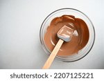 Small photo of Top view of glass bowl, spatula and tempering molten chocolate.The process of tempering chocolate and making chocolates