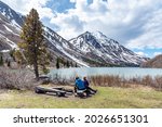 Hikers resting, sitting beside a isolated St Elias Lake in Kluane National Park during spring time, May with no other people. Snow capped mountains surrounding the scenic, Canadian view.