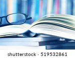 Close up opened book page and reading eyeglasses with blurry bookshelf background for education and publication concept