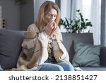 The sick woman is sitting on the couch at home, has a cough and fever, cold and runny nose