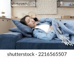 Young Asian woman lying sick on sofa at home. Calls on a mobile phone to the emergency room, to the doctor, to the hospital. Covered with a blanket, holding her stomach, she feels bad.