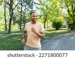 Cheerful and successful hispanic man jogging in the park, man running on a sunny day, smiling and happy having an outdoor activity.