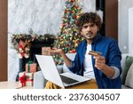 Small photo of Portrait of cheated unsatisfied man at home on New Year and Christmas holidays, hispanic man looking at camera with laptop rejected money transfer, using bank credit card.