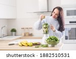 Woman standing in a kitchen squeezing lime into a blender full of fruit and vegetable.
