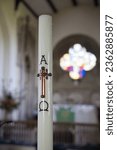 Small photo of A Candle with the crucifix and alpha and omega on it with a stained glass window and altar in soft focus in the background in St Pauls parish Church coleshill