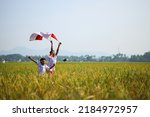 Indonesian school students wearing uniform are raising their hands while holding red white flag in the midst of the rice field. Celebrating independence day.