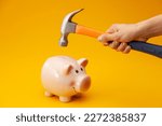 Small photo of A pink piggy bank is about to be hit by a hammer. A hand holding a hammer which is raised above a pink china piggy bank, with a shocked and apprehensive facial expression. Financial problem.