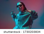 Small photo of Portrait of a cool boy child in a rap image, stylishly posing in a hoodie, sunglasses and a cap on a neon background.