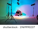 Creative team young girl and boy with laptop working in photostudio with photography equipment. Colorful neon light