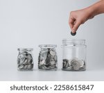 Woman hand with money coins in clear glass on white background, Business investment growth concept, saving concept, Hand putting coin in clear jar over white background. Copy space.