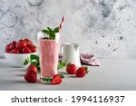 Strawberry smoothie or milkshake with berries and mint in tall glass on light grey background. Summer drink shake, milkshake and refreshment organic concept. Place for text.