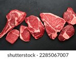 Raw prime steaks. Variety of fresh black angus prime meat steaks T-bone, New York, Ribeye, Striploin, Tomahawk cutting board on black or dark background. Set of various classic steaks. Top view. 