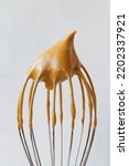 Small photo of close-up of Metal whisk with whipped coffee for dalgona coffee drink isolated on the white background. vertical. the whisk with whipped cream with copy space