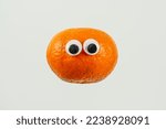 single orange satsuma tangerine with googly cartoon eyes isolated on a white background