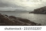 Small photo of View across Gruinard Bay in the Scottish Highlands looking towards Gruinard Island with rocky outcrops in the fore and midground, Highland mountains in the background and a cloudy sky lit by the sun.