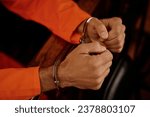 Small photo of Close-up of hands of young male suspect in metallic cuffs wearing orange jumpsuit