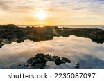 beautiful sea sunrise on a rocky sea coast with calm water , amazing cloudy sky and reflection on water surface
