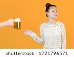 Small photo of The girl with undisguised joy agrees to take a mug of fresh beer from the hands of a man. Isolated on a yellow background. Beer alcoholism, female alcoholism. Youth and alcohol