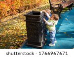 smart generation concept. two little cute babies are standing near the black street container in the park and throwing garbage there. another kid comes up behind. soft focus, background in blur.