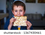Small photo of Cute Caucasian Jewish boy holding in his hands and taking a bite from a traditional Jewish matzo unleavened bread. Jewish Passover Pesach concept image.