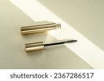 Mascara brush lies next to an open tube, on a beige background with shadows from sunlight. Copy space place for text cosmetic background