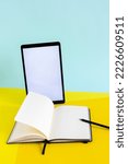 Small photo of Blank tablet and ope notebook with pencil on yellow and blue background, work desk with copy space, writer's workplace, online studying