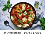 Pasta casserole with tomatoes and mozzarella cheese in a black iron pan on a light grey slate, stone or concrete background. Top view with copy space.