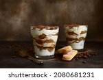 Tiramisu - traditional italian coffee dessert from mascarpone cheese and biscuit in a glass cup on a dark slate, srone or concrete background.