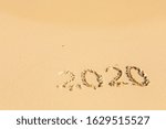 New Year 2020 is coming - inscription 2020 on a beach sand the wave is starting to cover the digits - Summer beach holiday 2020 season golden sand old year - message handwritten - empty copy space