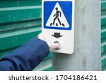 A hand in a silicone glove presses the crosswalk button. Protection on the street during the coronavirus pandemic. Pedestrian crossing sign.