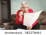 Small photo of Senior old woman shocked with the bills she receives, appalled and surprised