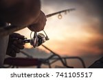 Fishing rod wheel closeup, man fishing with a beautiful sunrise behind him