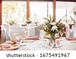White tablecloths with clear vases and white chrysanthemum and fern arrangements. Golden colored plates, peavh napkins, table numbers and mirror centerpieces.