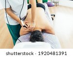 Small photo of Patient lying on the stretcher in the physiotherapy clinic is treated with diathermy treatment for muscle pain. Rehabilitation of a sick patient with muscle pain. Health concept