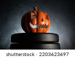 Small ceramic Halloween pumpkin on a dumbbell barbell weight plates. Healthy gym fitness lifestyle autumn or fall composition with decorative Jack-o'-lantern spooky laughing, scary head.
