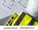 Home floor plans or building blueprint project, high-visibility clothing safety vest, spirit level and hard hat helmet for architect, construction worker, engineer contractor or interior designer.