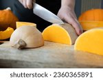 Woman cutting butternut squash pumpkin into slices with a kitchen knife on a wooden board. Fresh raw sliced pumpkins pieces. Preparing ingredients for a seasonal autumn fall dish, soup or pie.