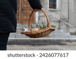 Small photo of Woman holding Easter basket for blessing in a church. Traditional woven wicker Paschal basket filled with various food, ready to be blessed by a priest as part of the Easter tradition.