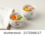 Small photo of Pot Steamed Hotchpotch Japanese Chawan Mushi on Cream Background with Narutomaki, Carrot, Corn, Crabstick, and Green Onion Topping