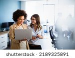 Happy multiethnic business women working together online on a laptop in corporate office.