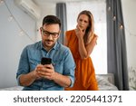 Small photo of Jealous woman spying boyfriend and watching his mobile phone. Couple cheating jealousy concept