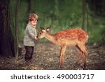 Cute little boy is feeding a baby fawn in the forest.  Image with selective focus and toning