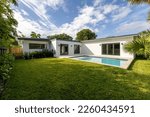 Beautiful backyard of elegant and modern house in the Nautilius neighborhood of Miami Beach, swimming pool, short grass, trees and tropical plants, blue sky in the background