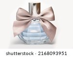 Small photo of A Gorgeous Beautiful Bottle Of Blue Perfume Of Women's Expensive Perfume With A Beige Fabric Bow. Perfume Bottle On A White Background.