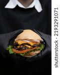 Small photo of Monster burger. Closeup view of a person wearing gloves, holding a multilayer burger with bread, meat, lettuce, tomato, cheddar cheese and ham.