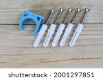 Plastic dowel expansion, screw many sets, and blue PVC pipe clamp hardware tools isolated on wooden background closeup.