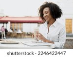 A beautiful curly-haired woman is smiling drinking cocoa coffee in a summer cafe.