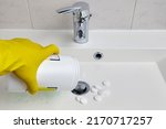 A man in yellow rubber gloves pours dry detergent granules into the bathroom sink. Housework and plumbing cleaning