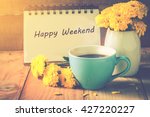 blue cup of coffee on wooden floor with yellow flower in white pot and happy weekend note on morning sunlight. vintage color tone, happy weekend concept.