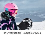 Small photo of Little girl snowboarder with equipment helmet and goggles outwear holding snowboard resting on top of ski slope in sunlight. 6-7 years girl at ski resort in sunny winter day. Free space for you text